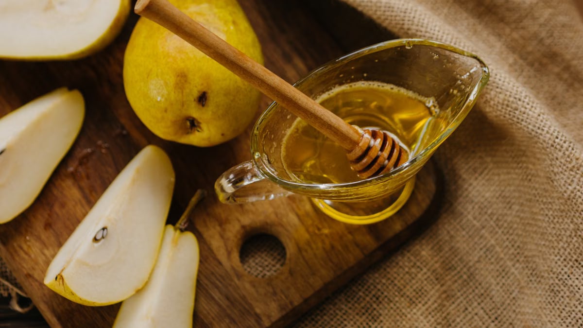 A rustic still life of sliced pears with honey drizzler on a wooden cutting board.